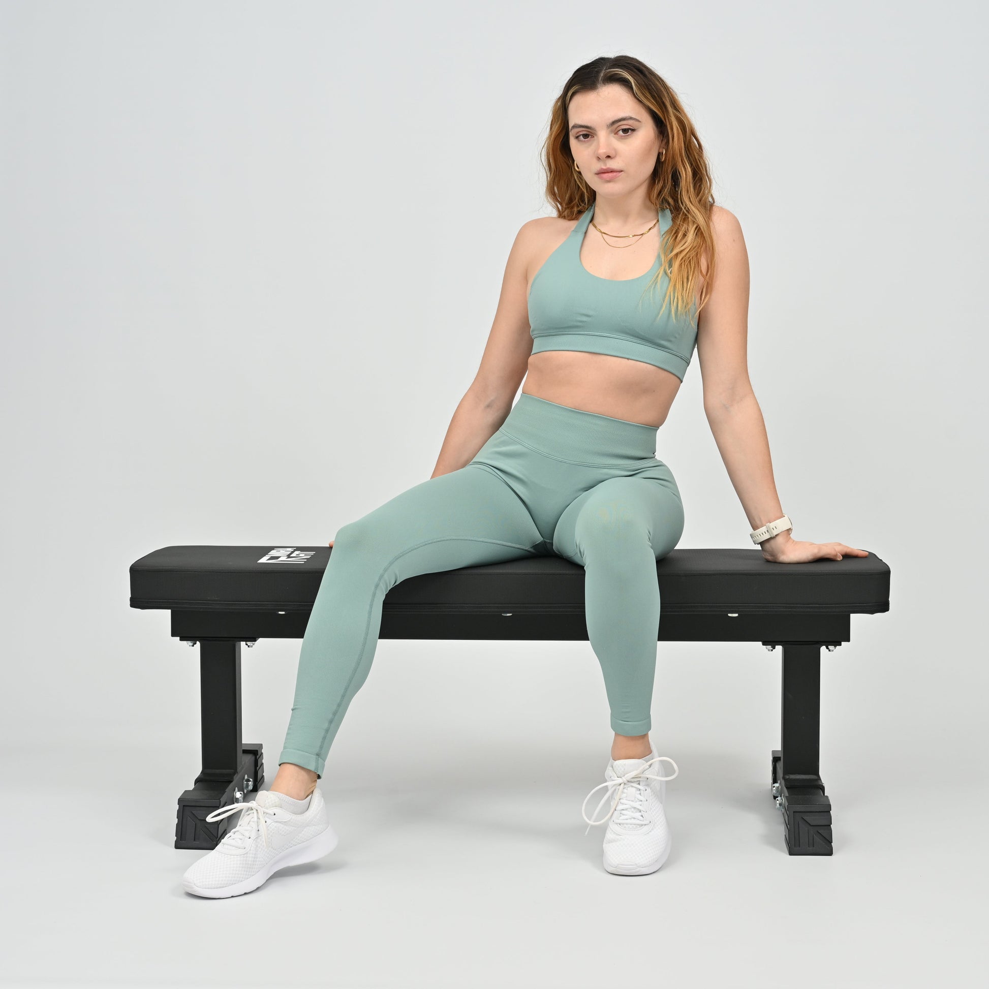 Woman in green athletic wear sitting on a black weight bench against a white background