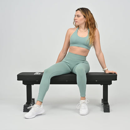 Woman in green athletic wear sitting on a black weight bench against a plain background