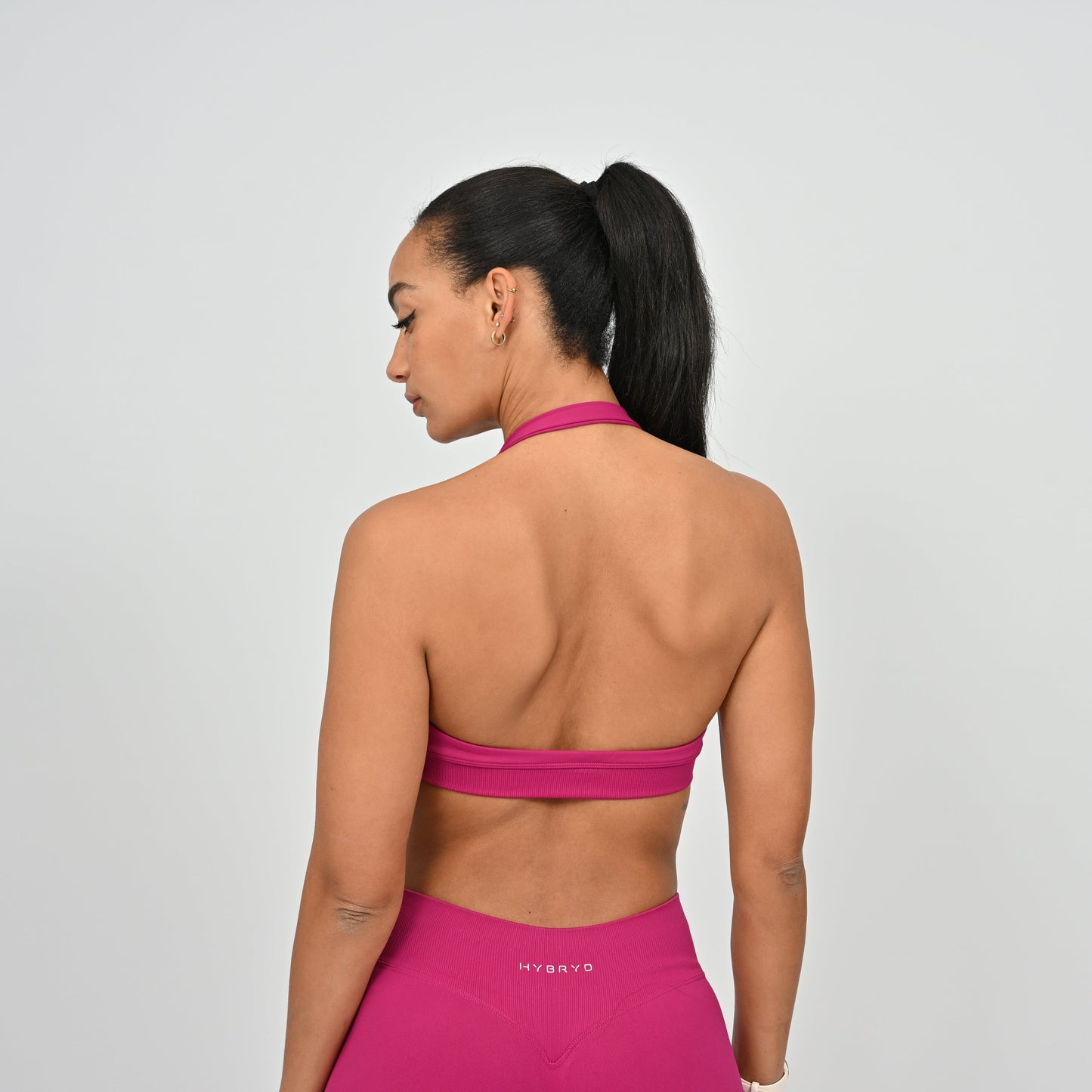 Woman wearing a pink sports bra and leggings with 'HYBRYD' branding on a gray background