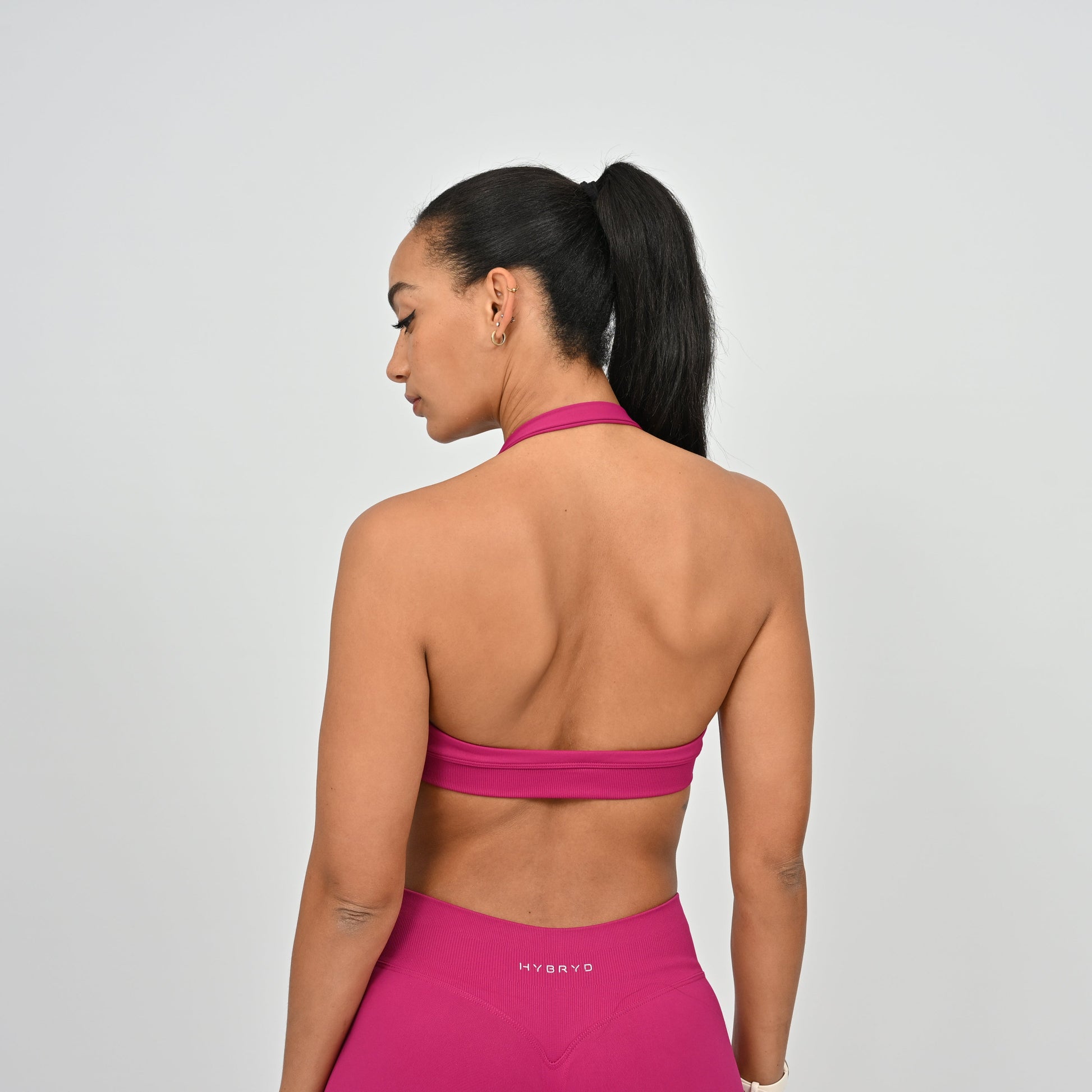 Woman wearing a pink sports bra and leggings with 'HYBRYD' branding on a gray background