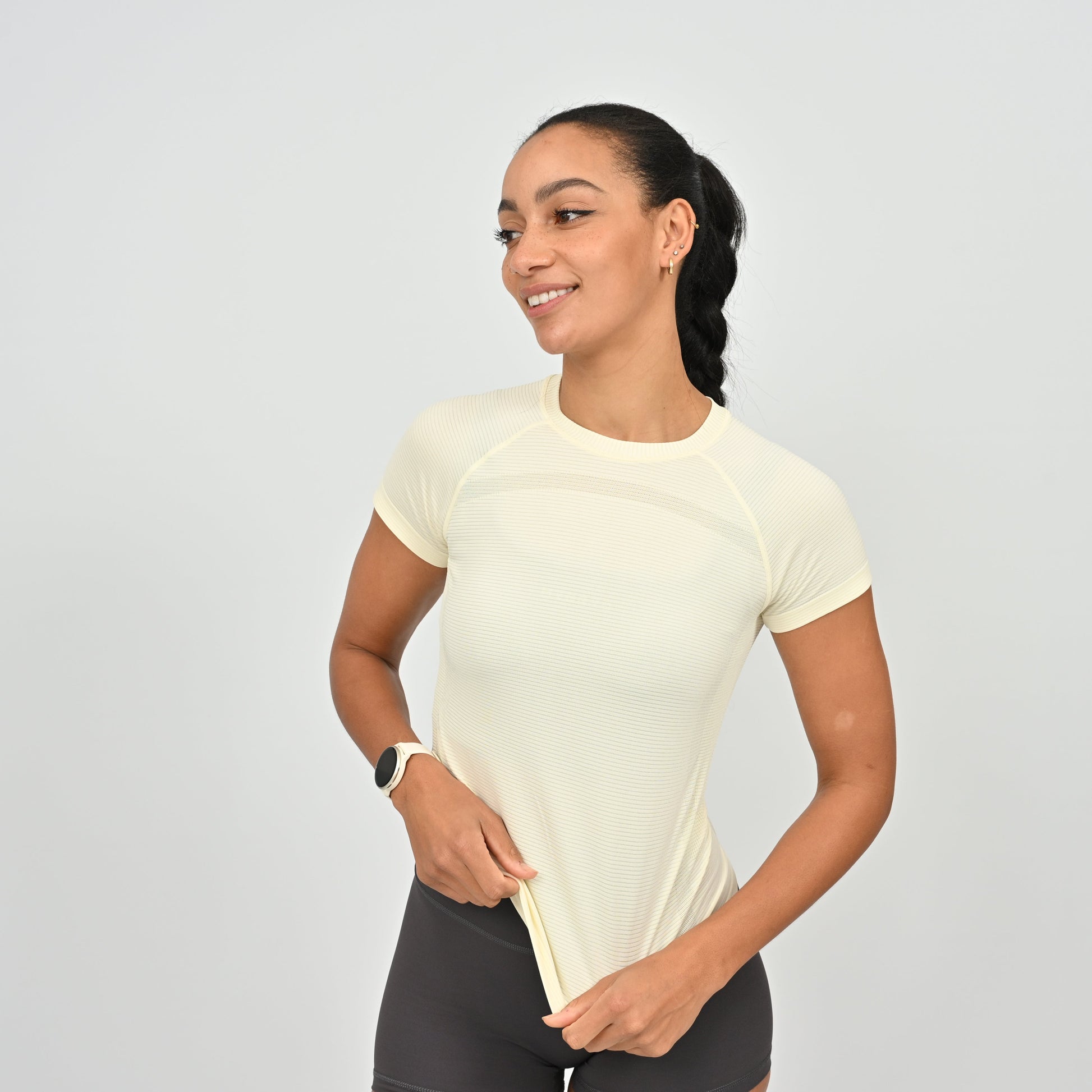 Woman wearing a yellow athletic shirt and black shortson a light gray background