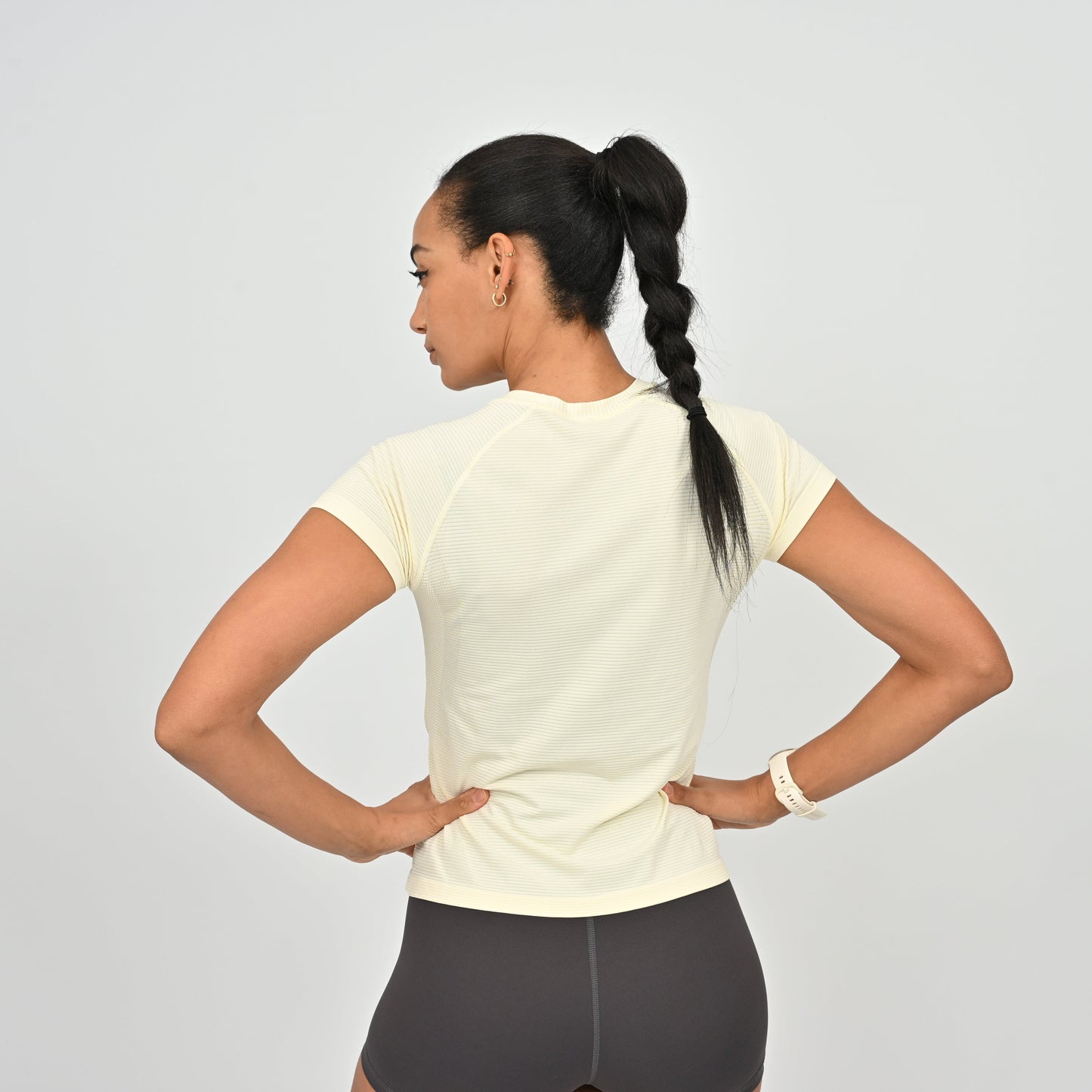 Woman wearing a light-colored athletic shirt and dark leggings on a plain background