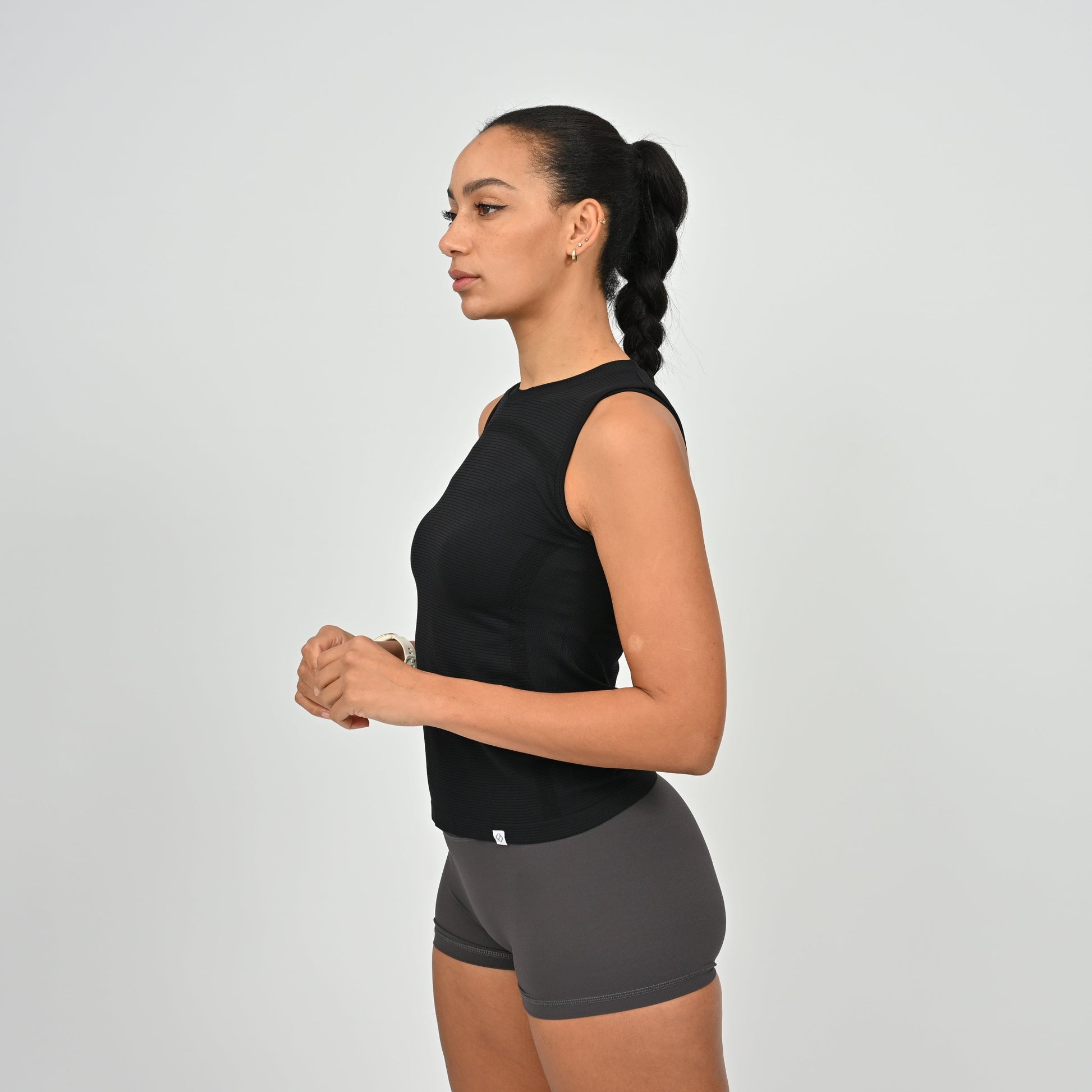 Woman wearing a black sleeveless actiewear top and gray shorts on a light gray background