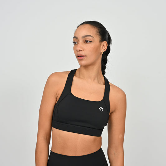 Woman wearing a black Hybryd sports bra with a logo on a light gray background
