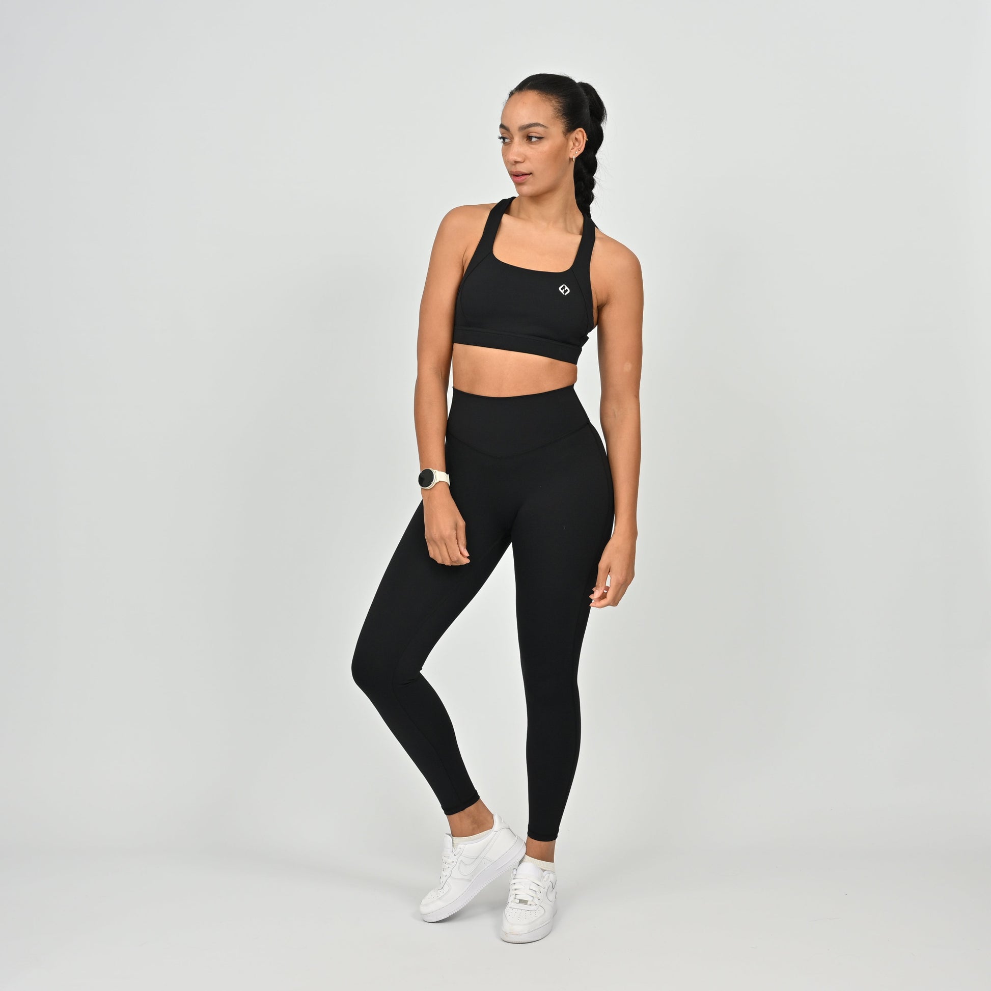 Woman wearing a black Hybryd sports bra and leggings set on a light gray background