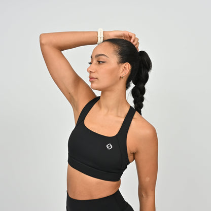 Woman wearing a black sports bra with a logo on a light gray background
