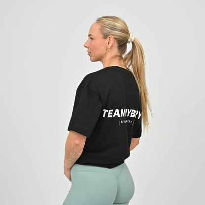 Woman wearing a black oversized t-shirt with 'TEAM HYBRYD' text on the back against a plain background