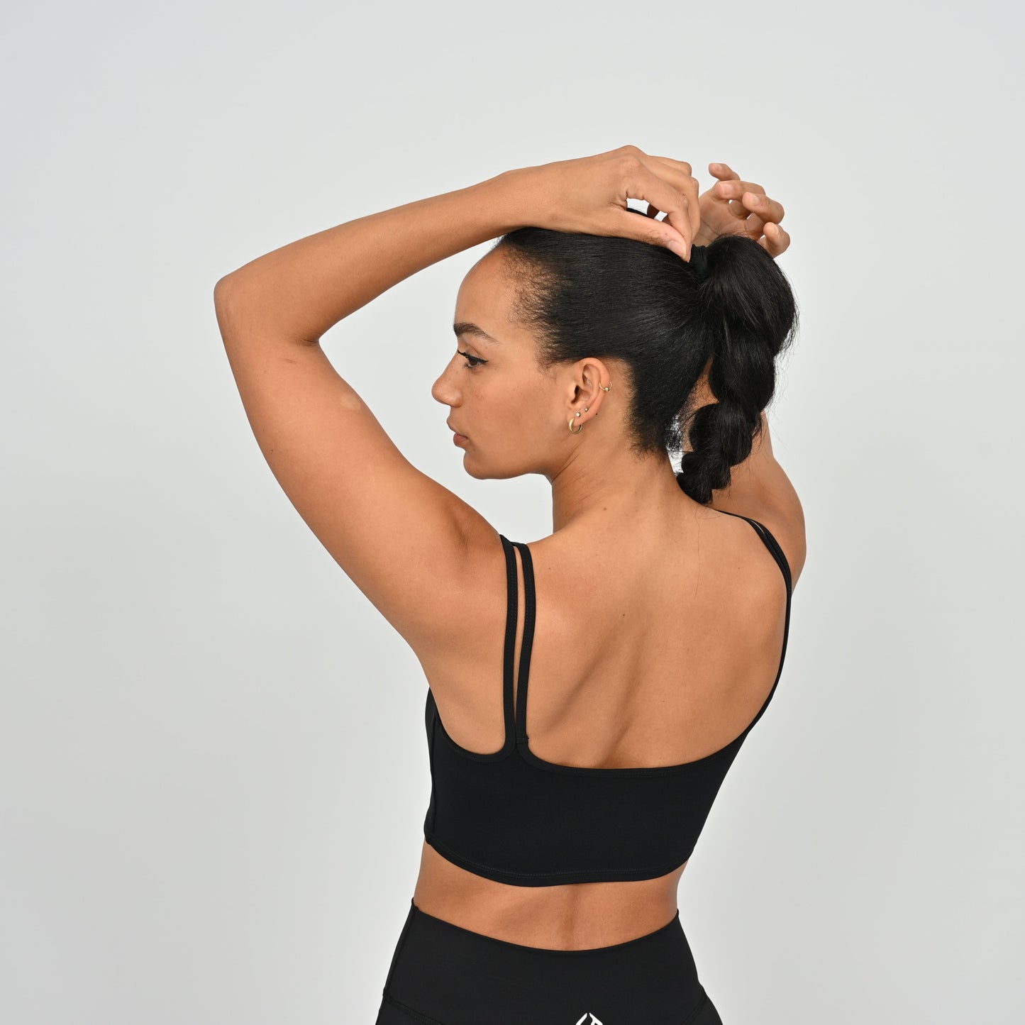 Woman wearing a Hybryd black gymwear bra and leggings against a light gray background