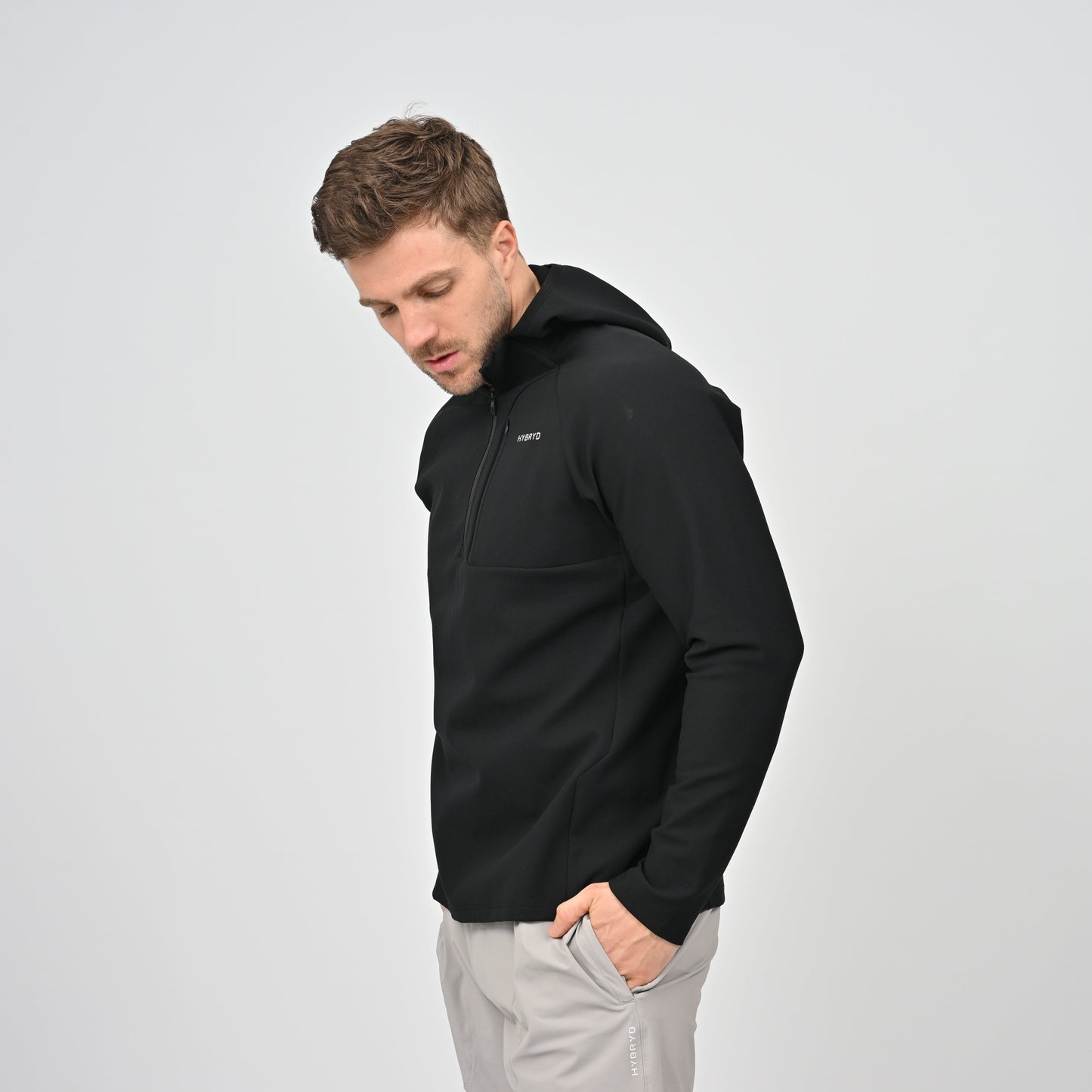 Man wearing a black Hybryd jacket with a logo on a light gray background