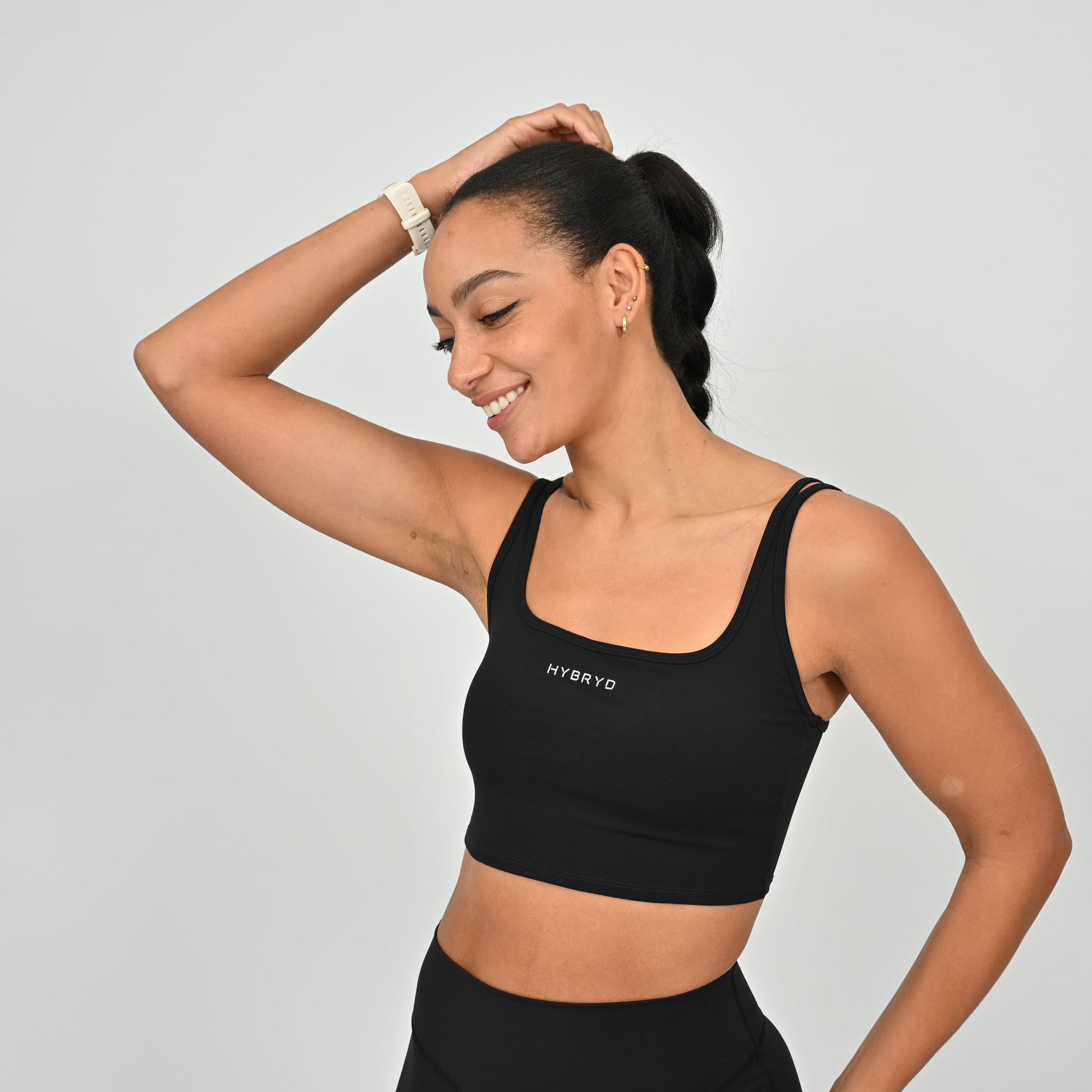 Woman wearing a black sports bra with 'HYBRYD' logo on a light gray background