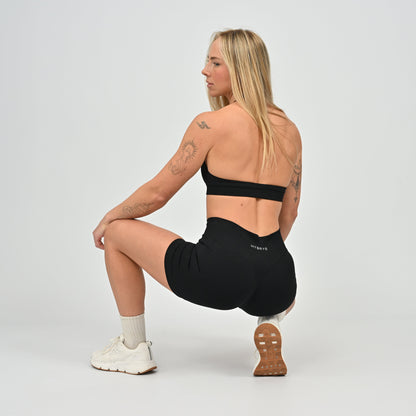 Woman in black hybryd gym set performing a squat on a light gray background