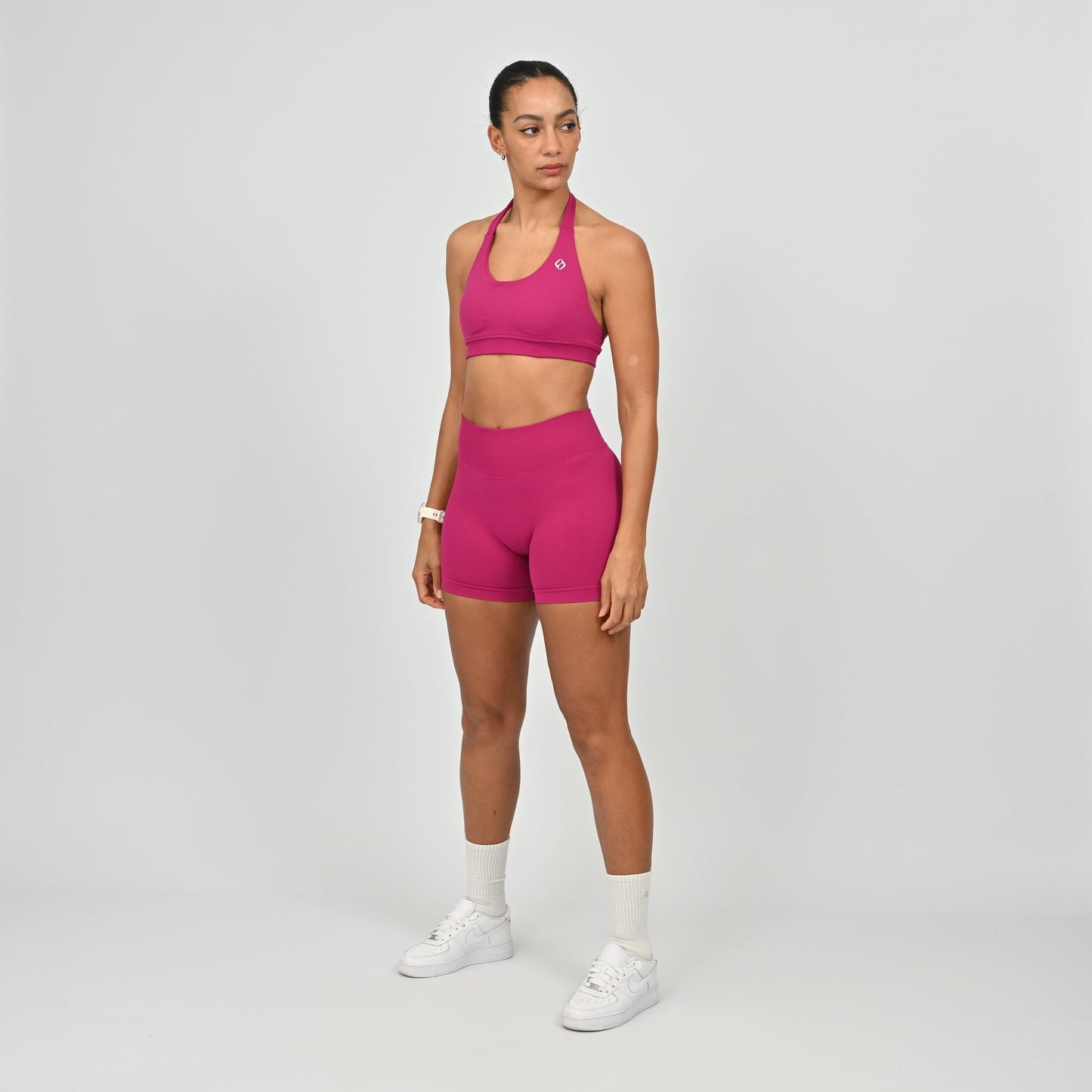 Woman wearing a pink Hybryd sports bra and booty shorts set on a gray background