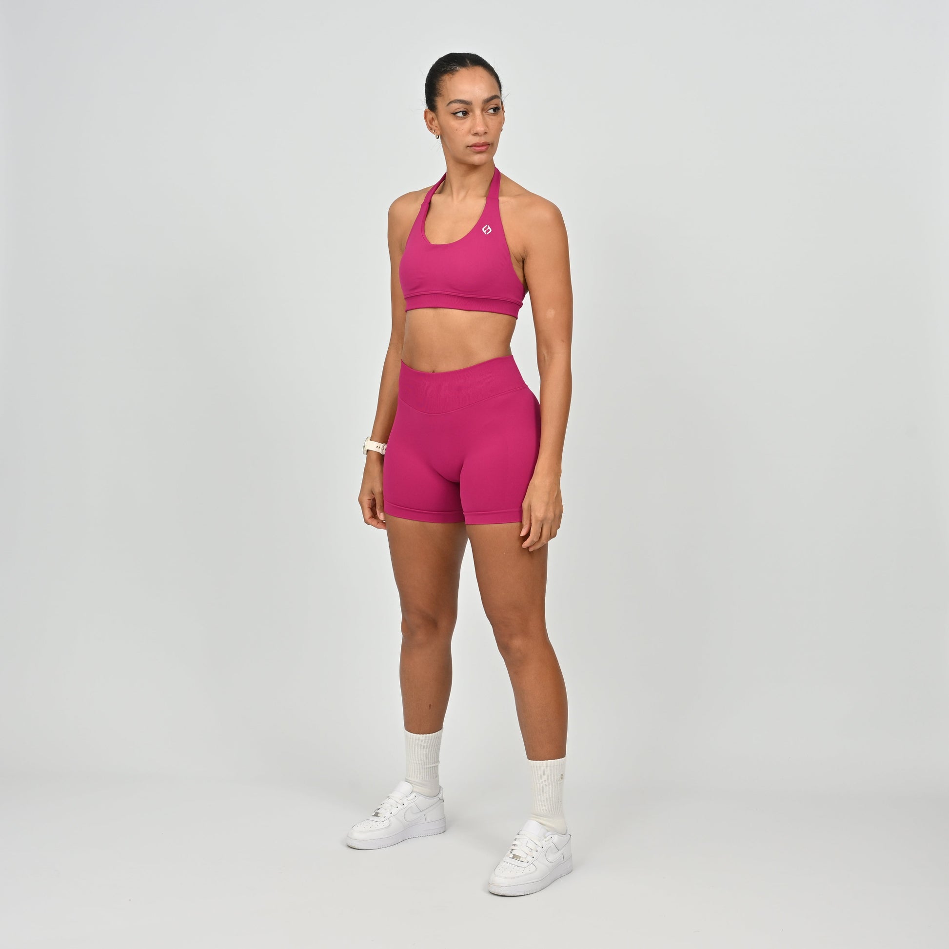 Woman wearing a pink Hybryd sports bra and booty shorts set on a gray background