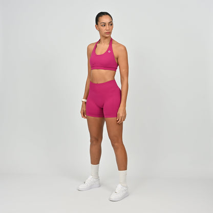 Woman wearing a pink Hybryd sports bra and booty shorts set on a gray background