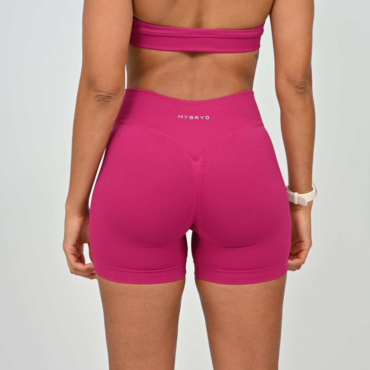 Person wearing pink high-waisted shorts with 'HYBRID' branding on a gray background
