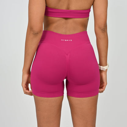 Person wearing pink high-waisted shorts with 'HYBRID' branding on a gray background