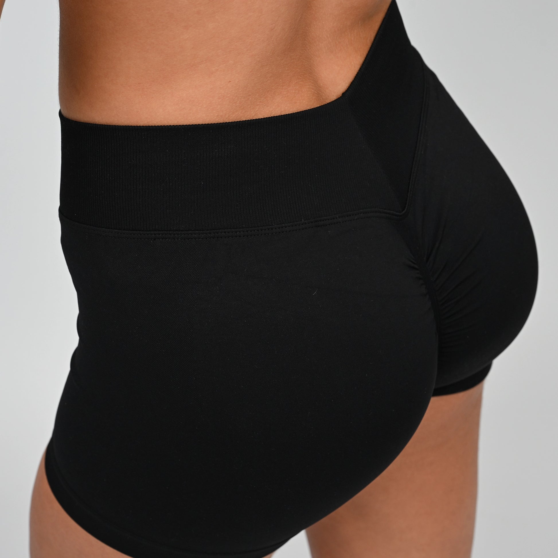 Black athletic scrunch bum and v dip waistband shorts worn by a Hybryd athlete on a gray background