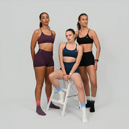 Three women wearing athletic gym wear and colorful ombre Hybryd socks against a plain background