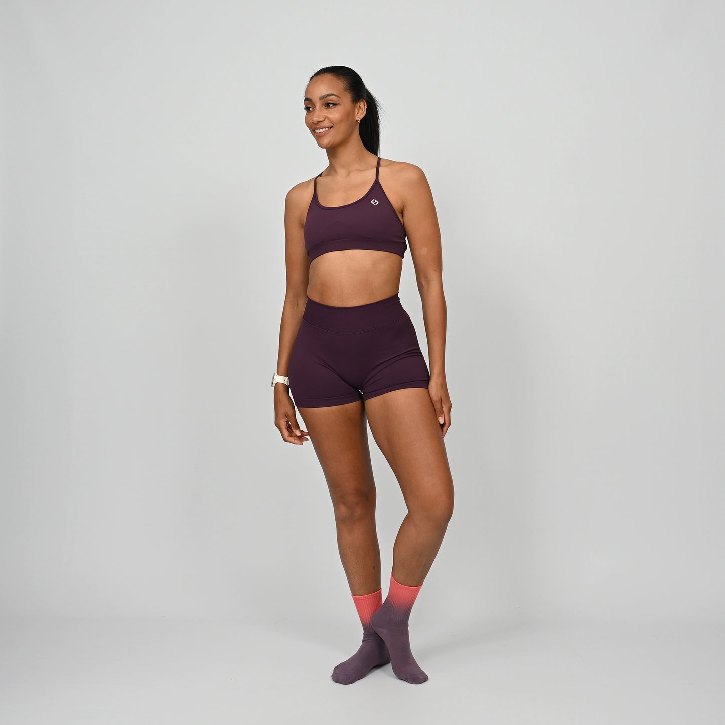 Crossfit athlete wearing a maroon minimal Hybryd sports bra and booty shorts set on a gray background