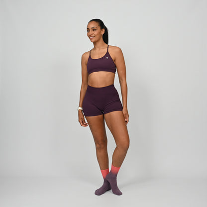 Crossfit athlete wearing a maroon minimal Hybryd sports bra and booty shorts set on a gray background