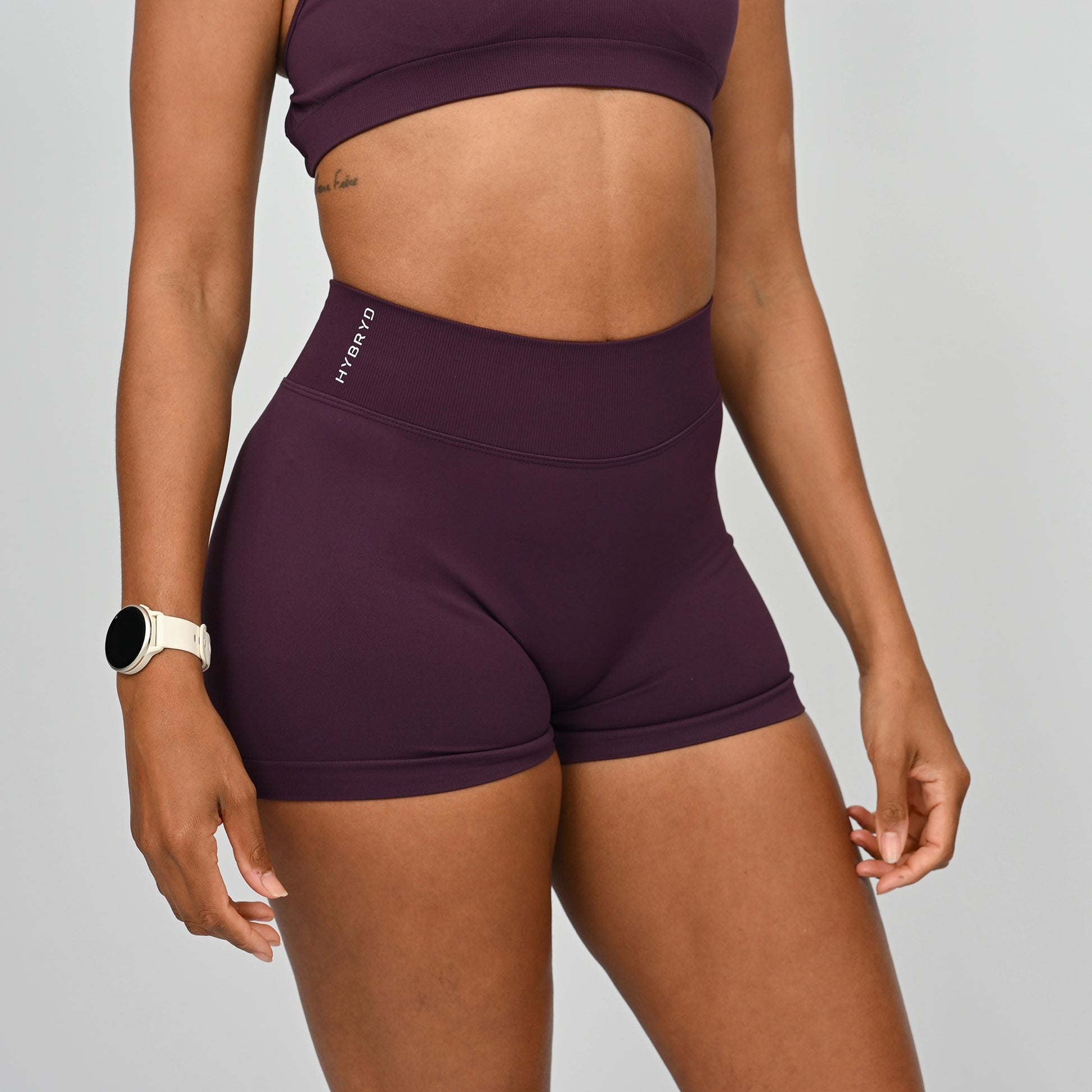 Crossfit athlete wearing purple matching Hybryd gym set with shorts and minimal bra with a gray background