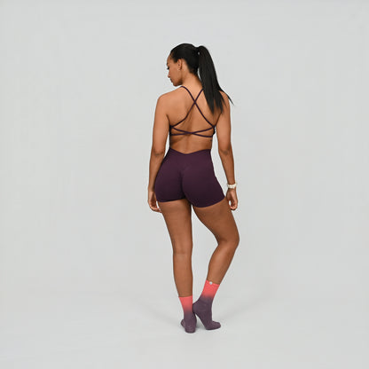 Hybryd athlete wearing a dark purple gym set with a strappy back design on a light gray background