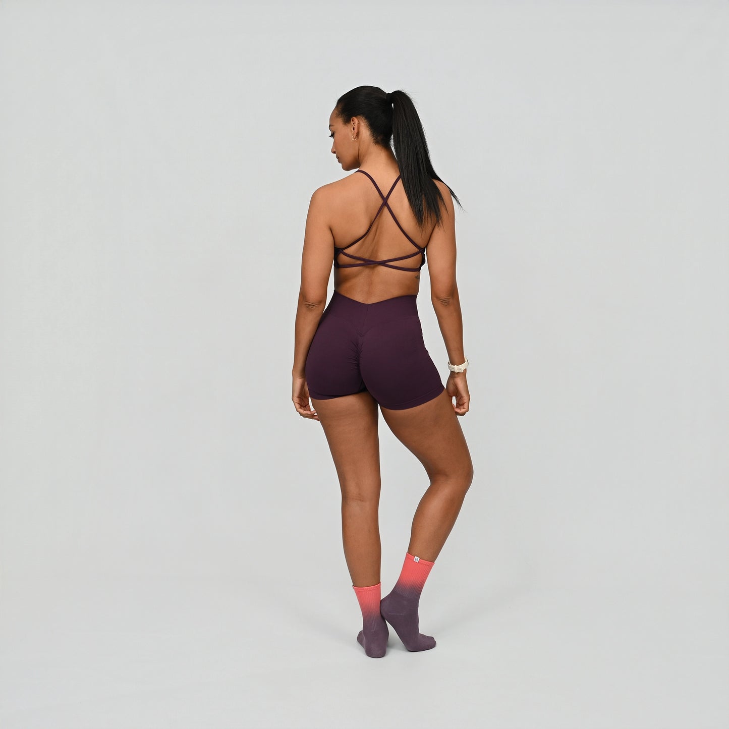 Hybryd athlete wearing a dark purple sports training outfit with a strappy back design and scrunch bum on a light gray background