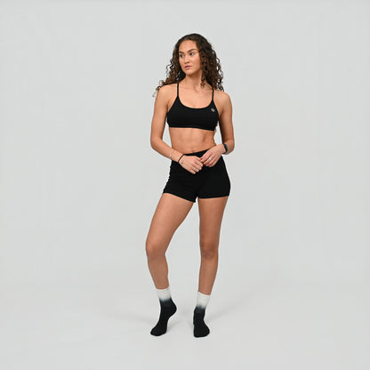 Hybryd athlete wearing a black minimal sports bra and bum scrunch shorts on a gray background