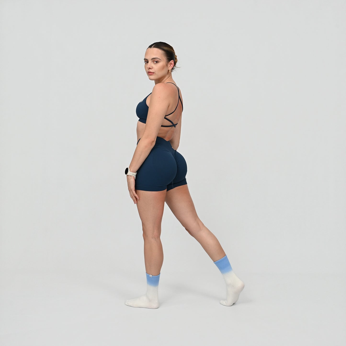 Person wearing a navy blue gym set with a minimal sports bra and shorts on a light gray background