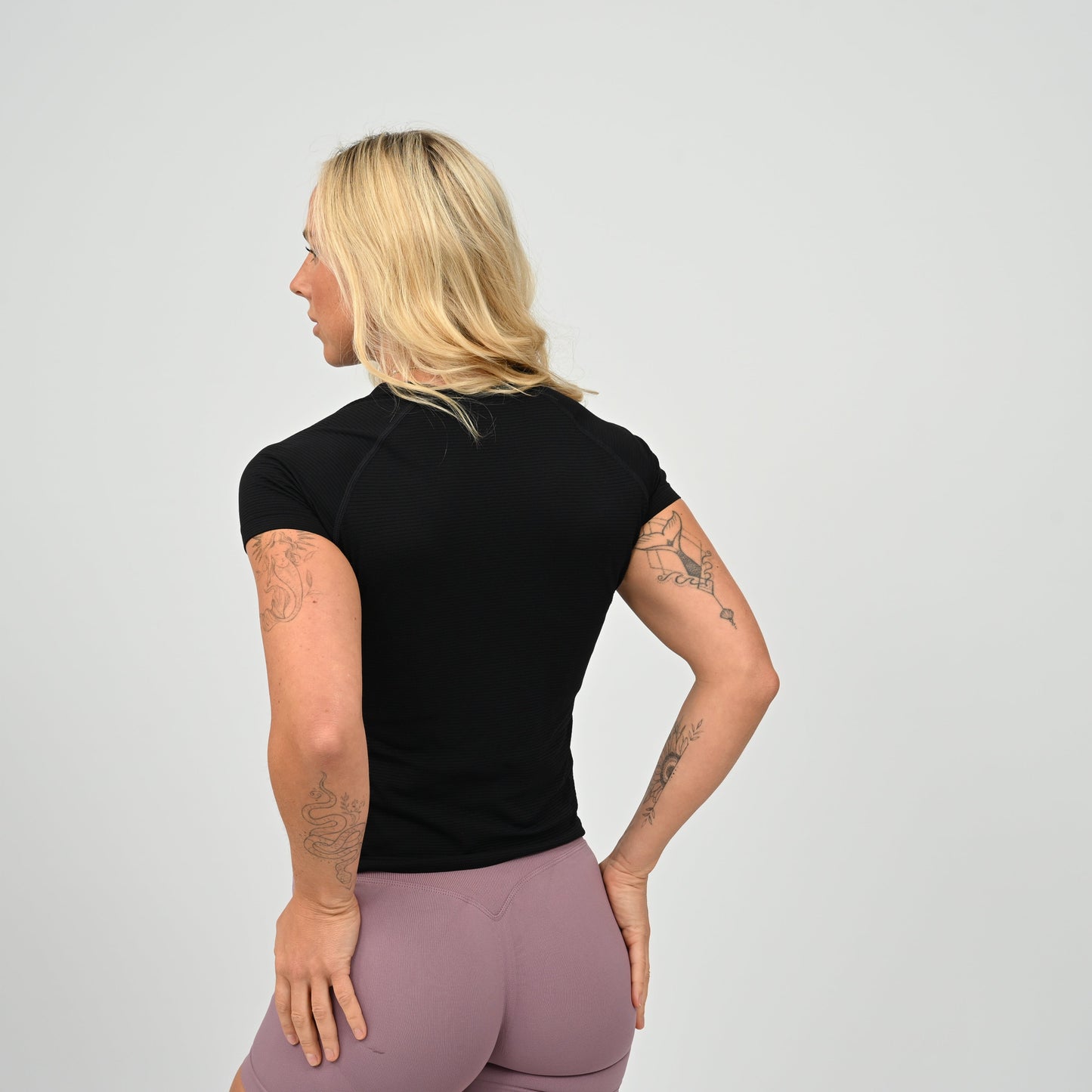Woman wearing a black stretchy, fitted  gym t-shirt with a Hybryd logo and booty shorts against a plain background