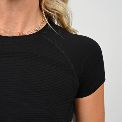 Close-up of an athlete wearing a black Hybryd ribbed top with a plain background