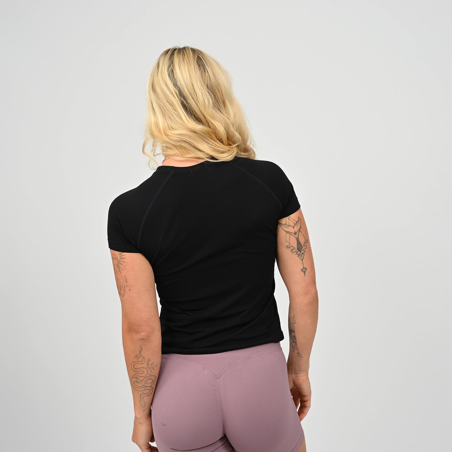 Crossfit athlete wearing a black workout  t-shirt with raglan sleeves and pink leggings from behind on a plain background