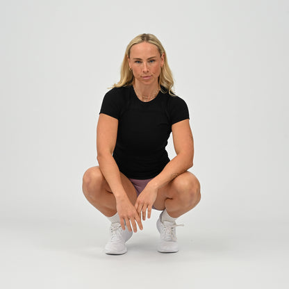 Woman in black stretchy activewear t-shirt made by Hybryd and white sneakers posing on a plain background