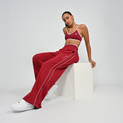 Gym Athlete wearing a crimson red Hybryd minimal sports bra and wide leg joggers with white piping on a light gray background