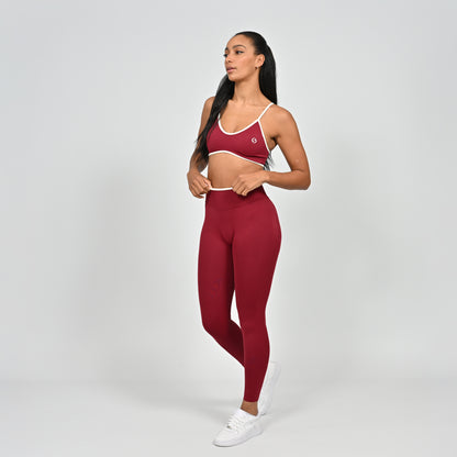 Gym Athlete wearing a crimson red Hybryd minimal sports bra and matching cinch bum leggings with white piping on a light gray background