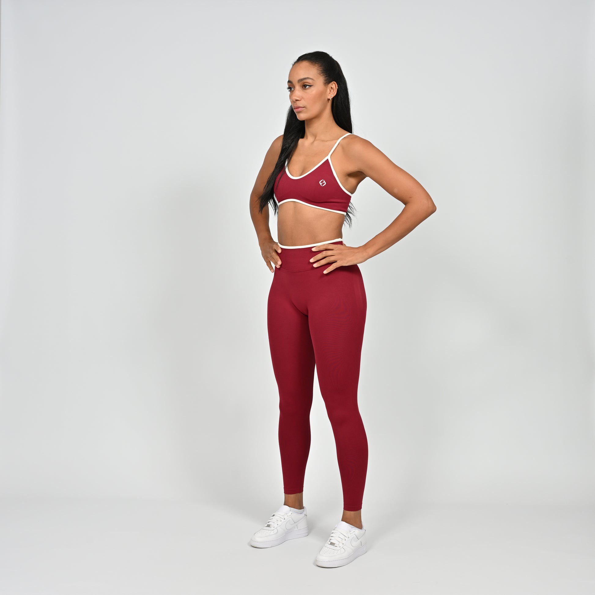 Gym Athlete wearing a crimson red Hybryd minimal sports bra and matching cinch bum leggings with white piping on a light gray background