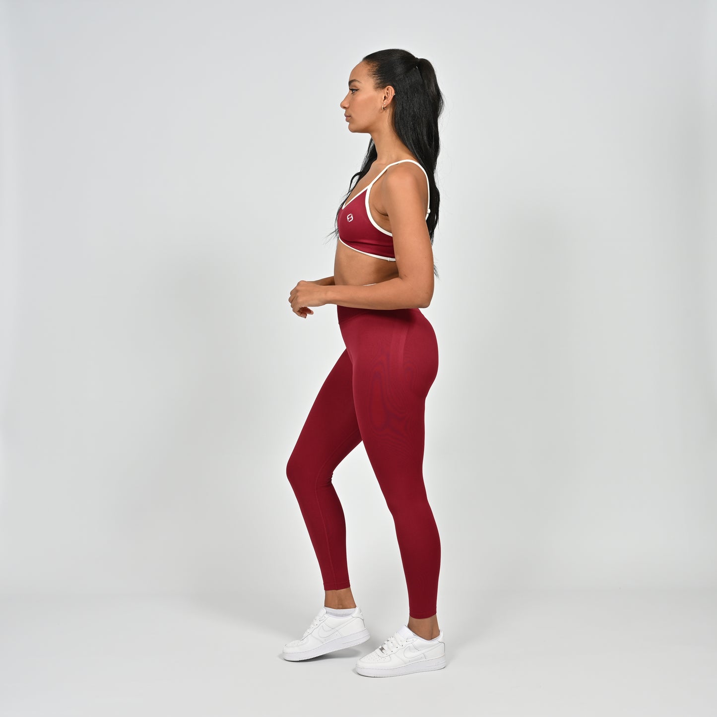 Gym Athlete wearing a crimson red Hybryd minimal sports bra and matching cinch bum leggings with white piping on a light gray background