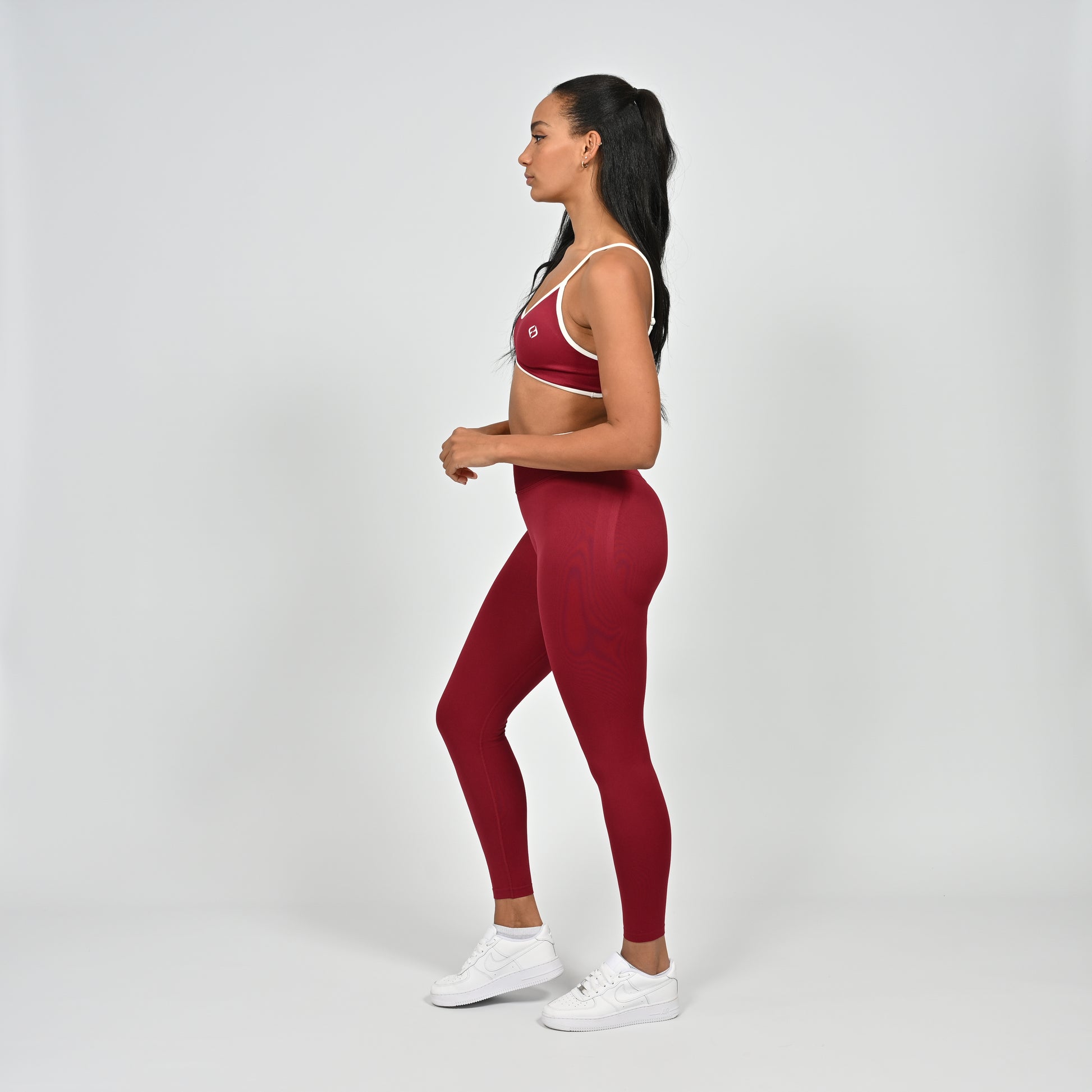 Gym Athlete wearing a crimson red Hybryd minimal sports bra and matching cinch bum leggings with white piping on a light gray background