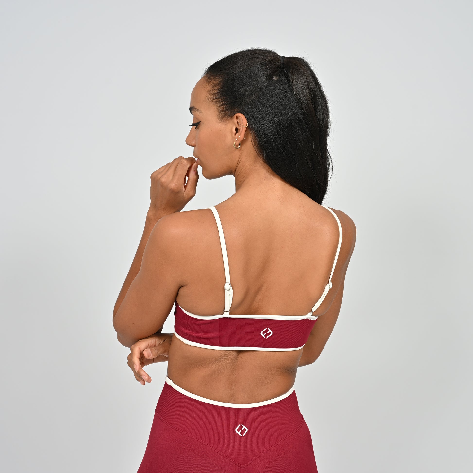 Gym Athlete wearing a crimson red Hybryd minimal sports bra and matching cinch bum leggings on a light gray background