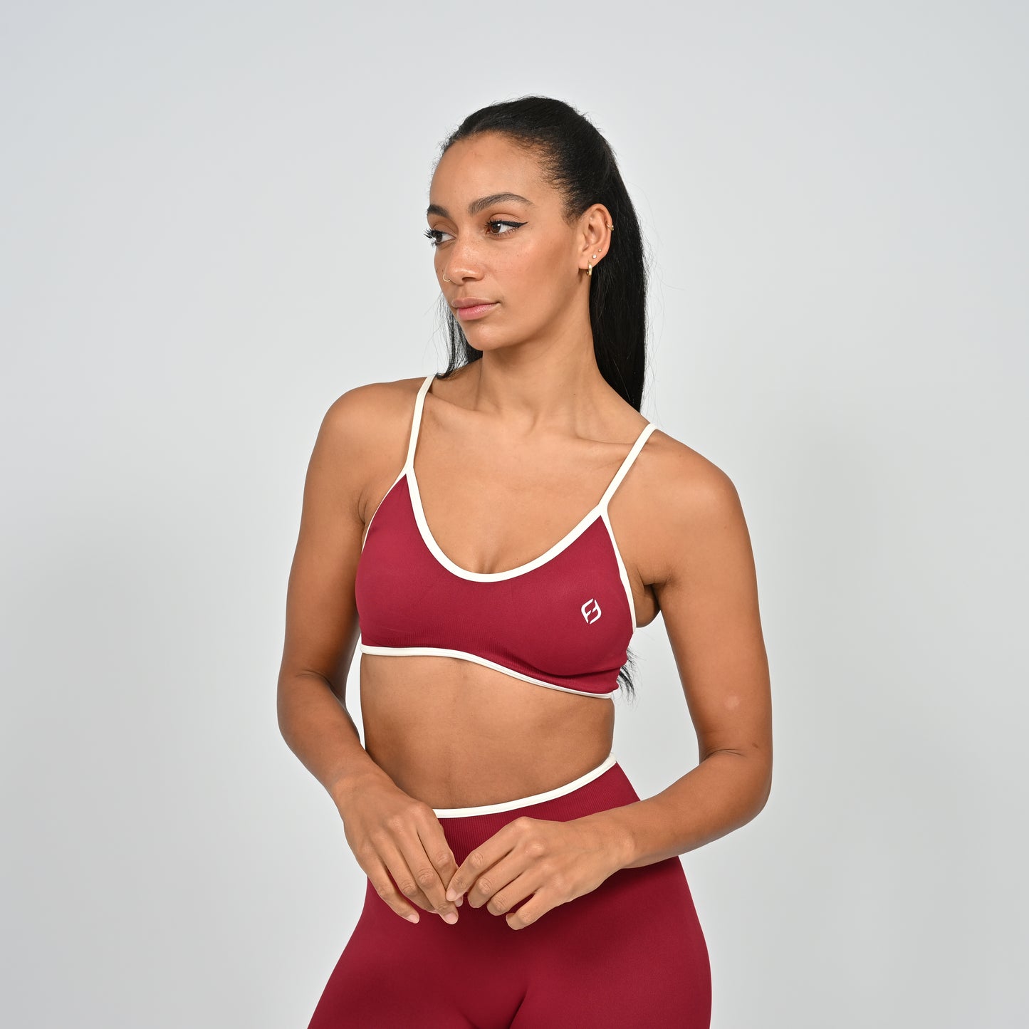 Gym Athlete wearing a crimson red Hybryd minimal sports bra and matching cinch bum leggings on a light gray background