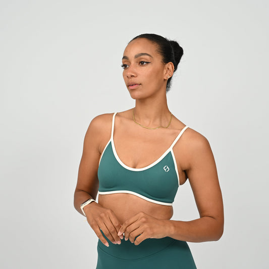 Athlete wearing a jade Hybryd green minimal sports bra and matching leggings on a light gray background
