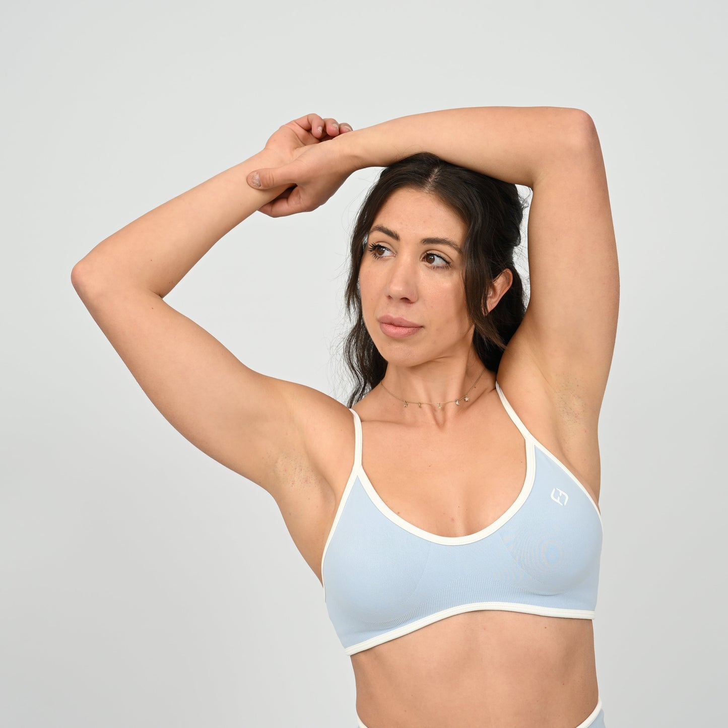 Crossfit girl wearing a powder blue minimal sports bra with white piping and removable pads. Front view on a white background. Made by the gymwear brand Hybryd.