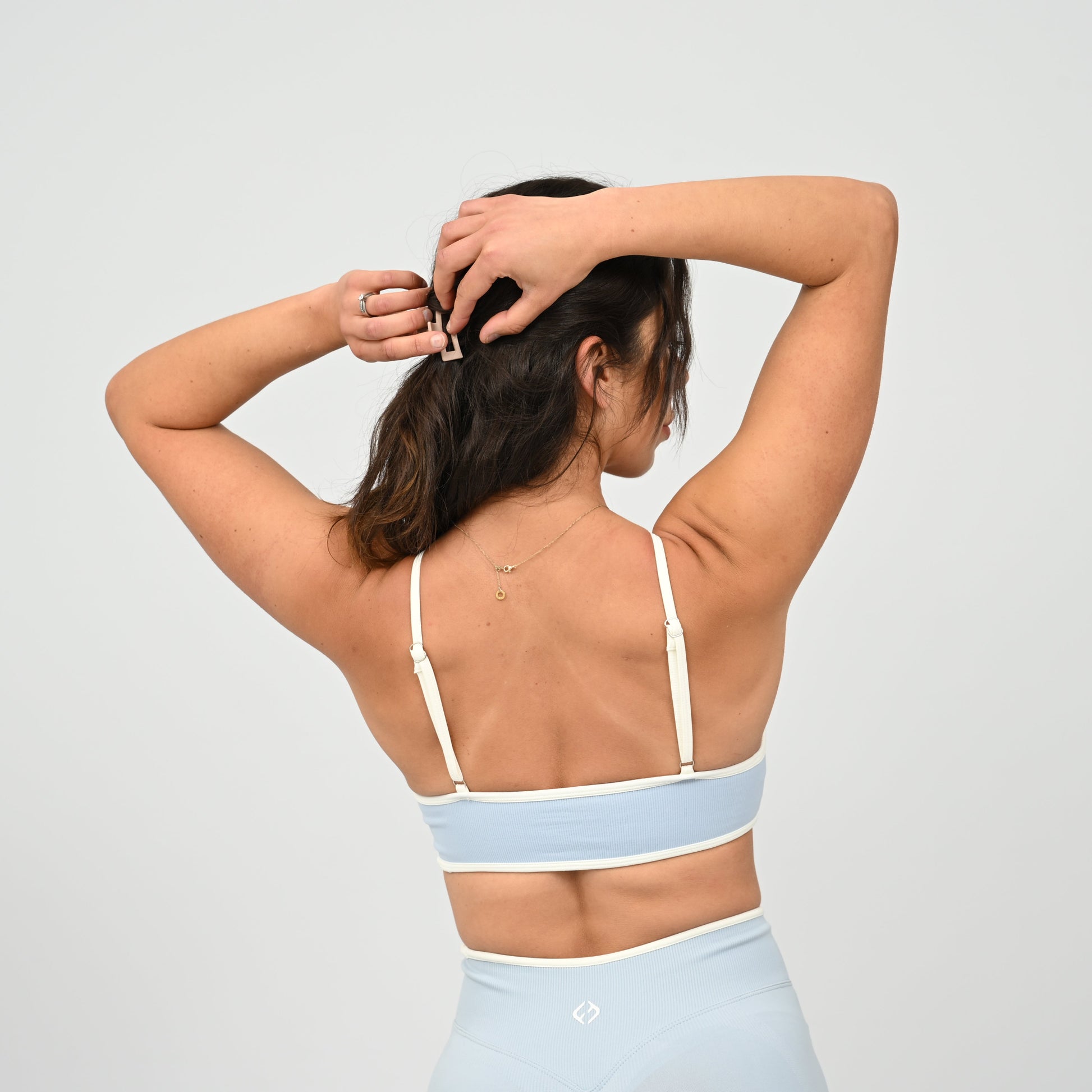 Crossfit girl wearing a powder blue minimal sports bra with white piping and removable pads. Rear view on a white background. Made by the gymwear brand Hybryd.