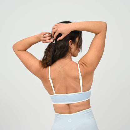 Crossfit girl wearing a powder blue minimal sports bra with white piping and removable pads. Rear view on a white background. Made by the gymwear brand Hybryd.