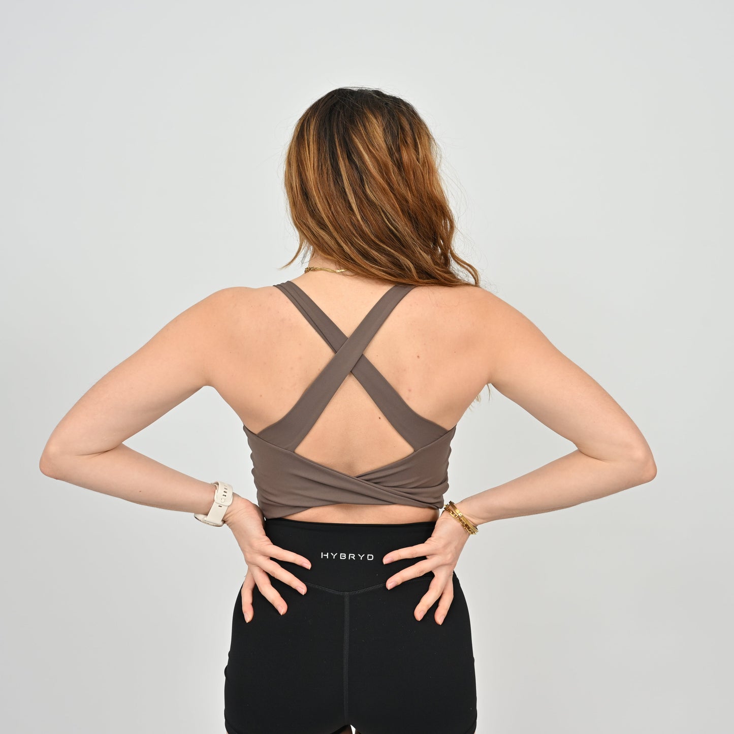 Woman wearing a brown sports bra and black leggings with 'HYBRYD' branding on a light gray background