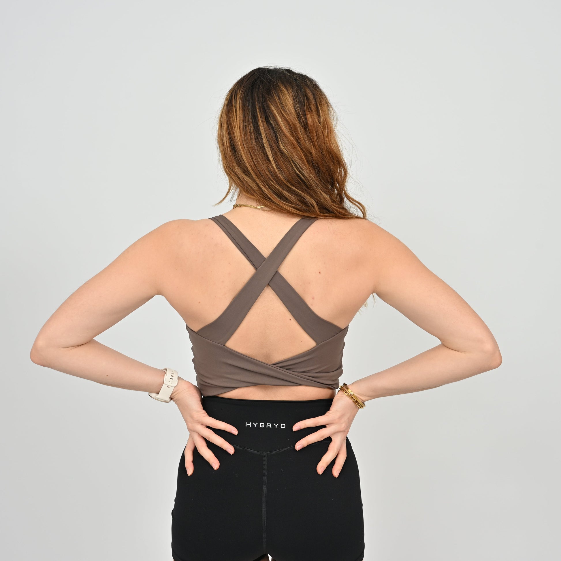 Woman wearing a brown sports bra and black leggings with 'HYBRYD' branding on a light gray background