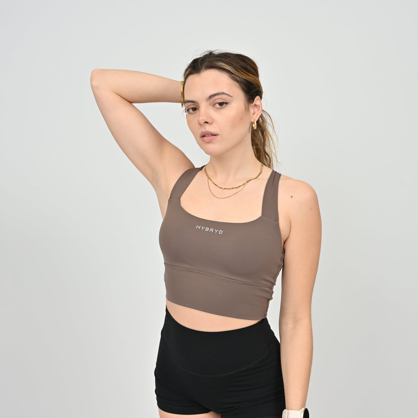 Woman wearing a brown sports bra with 'HYBRYD' branding on a gray background