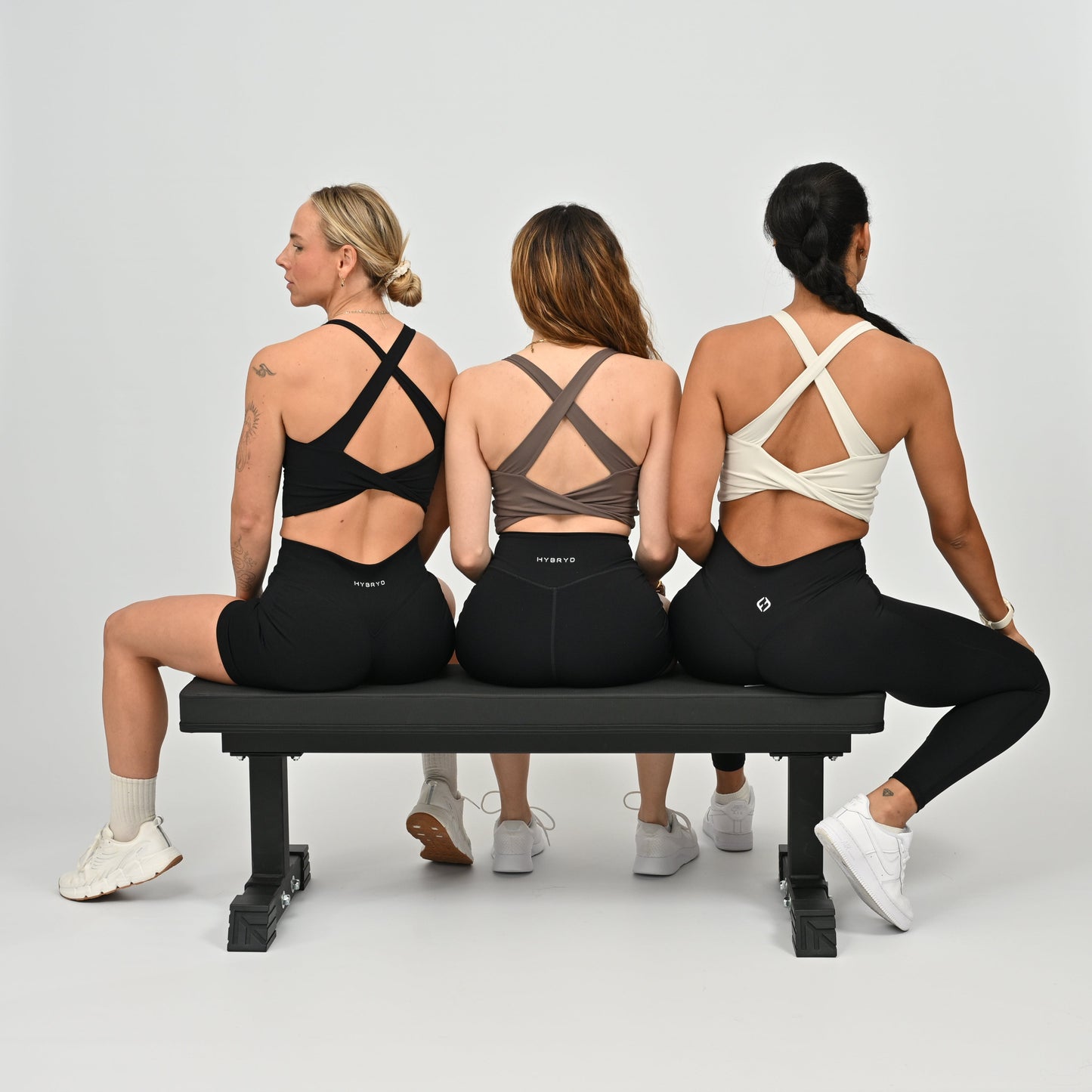Three women sitting on a bench wearing black leggings with visible HYBRYD branding.