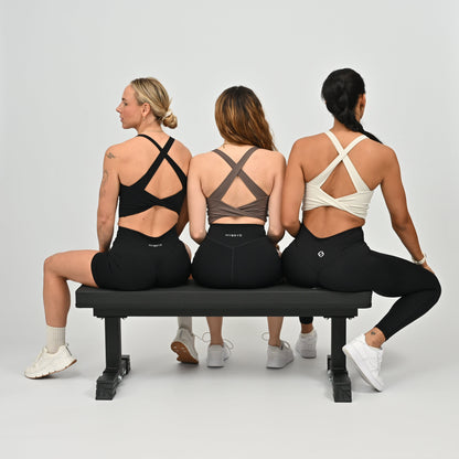 Three women sitting on a bench wearing black leggings with visible HYBRYD branding.