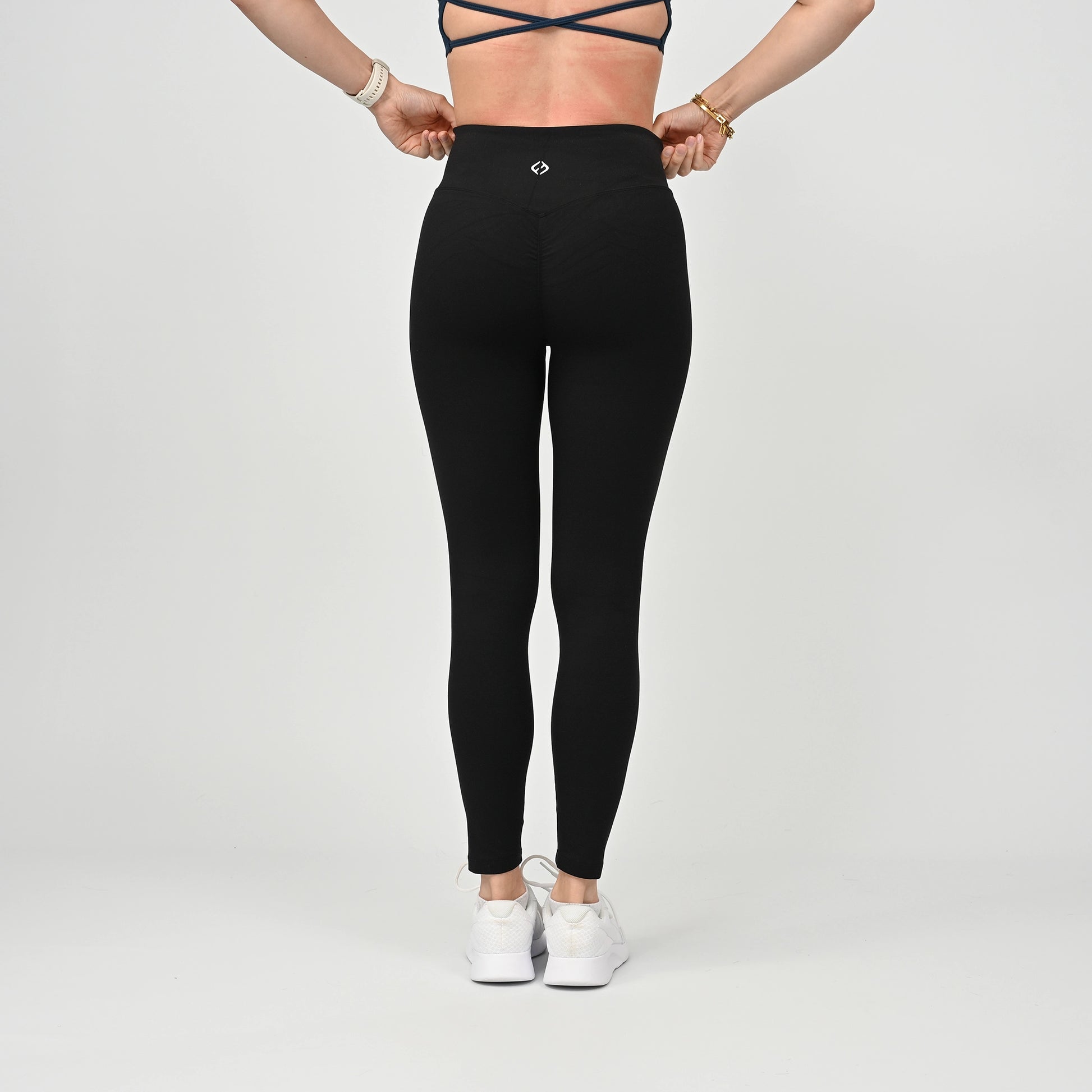 Person wearing black athletic active wear cinched bum leggings with a white logo on a light gray background
